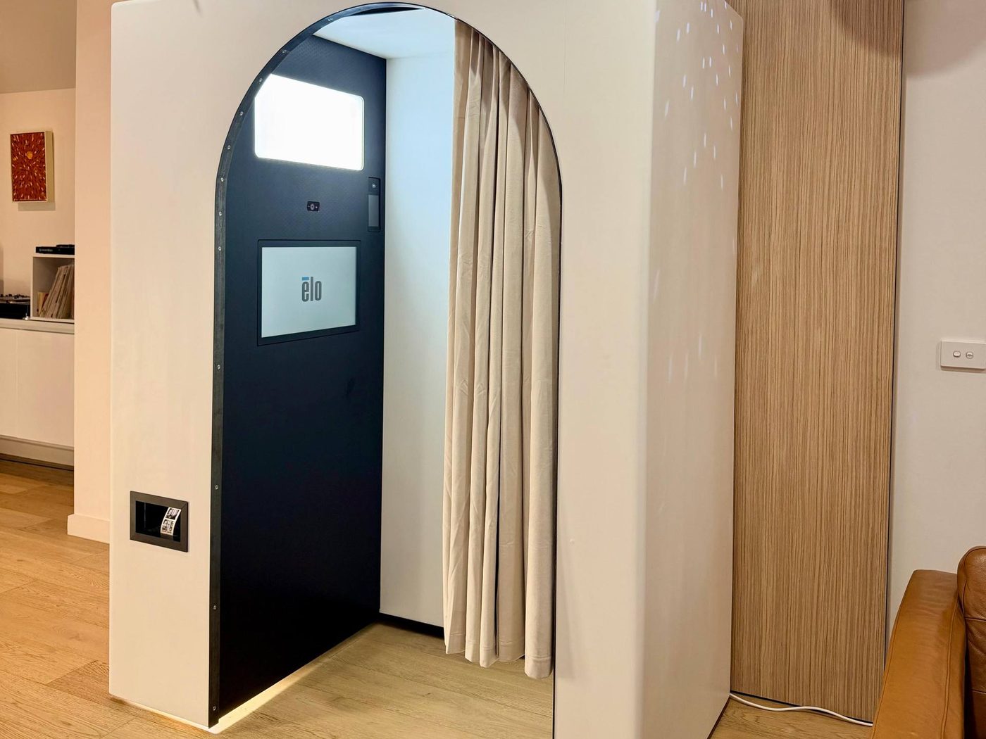 Inside the booth: a big soft light panel above a touchscreen, a curtain down one side, and the print slot on the outside wall.